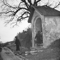 Kálvária, előtérben egy stáció-fülke a Szirtes út közelében, háttérben a fák között a Kálvária kápolna.